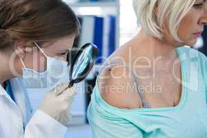 Dermatologist examining mole of female patient with magnifying glass