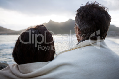 Rear view of couple wrapped in shawl on beach