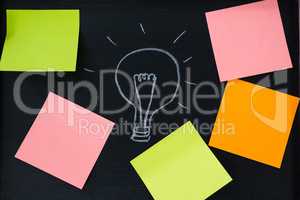 Bulb on chalkboard with blank multicolored adhesive note