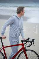 Thoughtful man standing with bicycle on beach