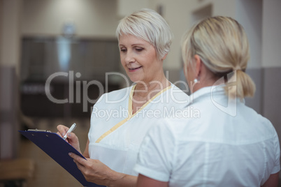 Two nurse having discussion over clipboard in corridor