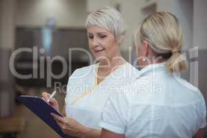 Two nurse having discussion over clipboard in corridor