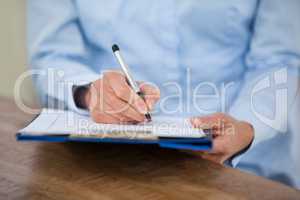 Mid section of doctor writing on clipboard