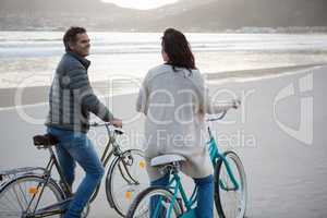 Couple standing on bicycle interacting with each other on beach