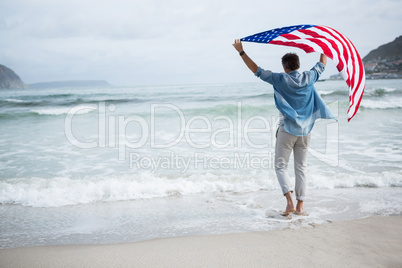 Rear view of man holding american flag on beach