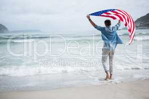 Rear view of man holding american flag on beach