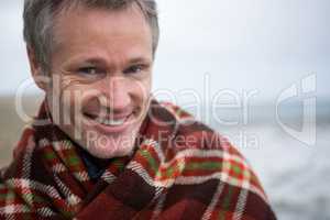 Smiling man wrapped in shawl at the beach