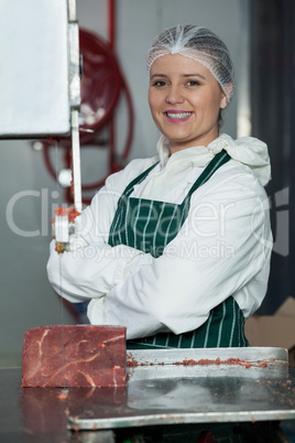 Portrait of female butcher with arms crossed standing near band saw machine