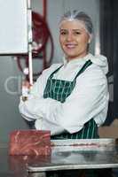 Portrait of female butcher with arms crossed standing near band saw machine