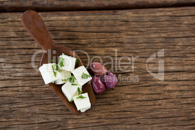 Cheese cubes garnished with herbs and olives on wooden spoon