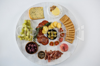 Variety of cheese with grapes, olives, salami, and crackers on wooden board