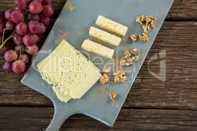Pieces of cheese, walnut and grapes on chopping board