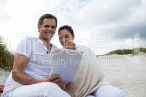 Happy couple using digital tablet on beach