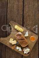 Variety of cheese, brown bread and knife on wooden board