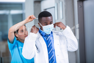 Nurse helping doctor to put on surgical mask