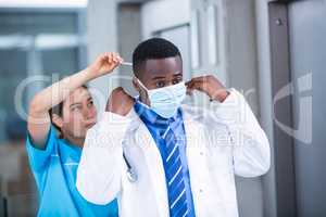 Nurse helping doctor to put on surgical mask