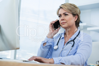 Female doctor talking on mobile phone while working over computer