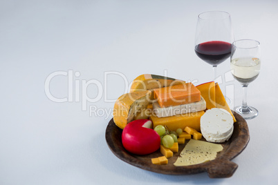 Glasses of wine with variety of cheese on wooden plate