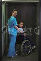Portrait of female nurse assisting patient on wheelchair in corridor