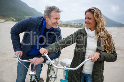 Happy couple standing with bicycle on beach