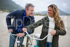 Happy couple standing with bicycle on beach