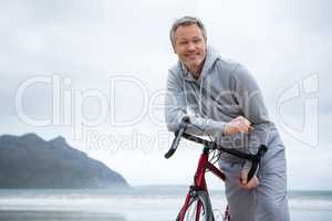 Portrait of happy man leaning on bicycle at beach