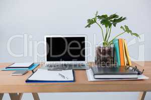Laptop with mobile phone, clipboard, diary and pen on table