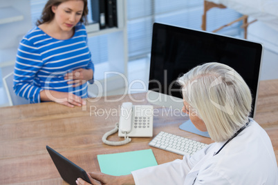 Doctor discussing with pregnant patient over digital tablet