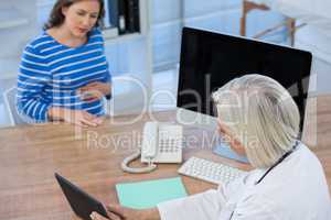 Doctor discussing with pregnant patient over digital tablet