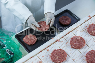 Butcher arranging hamburger patty on tray