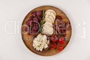 Crispy biscuits, cherry tomatoes, grapes and bowl of cheese on wooden board