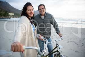 Portrait of couple standing with bicycle on beach