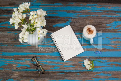 Cup of coffee, flowers in flowerpot, notepad and spectacles placed together