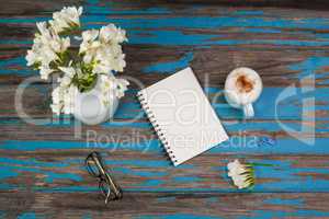 Cup of coffee, flowers in flowerpot, notepad and spectacles placed together