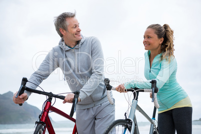 Happy couple standing with bicycle on beach