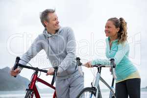 Happy couple standing with bicycle on beach