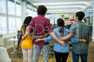 Team of business executives with arms around in office at desk