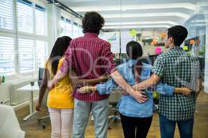 Team of business executives with arms around in office at desk