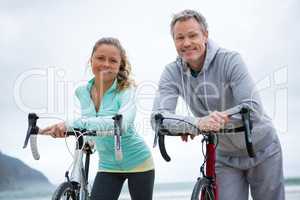 Portrait of happy couple leaning on bicycle at beach