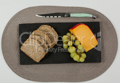 Brown bread, grapes and gouda cheese with knife on slate board