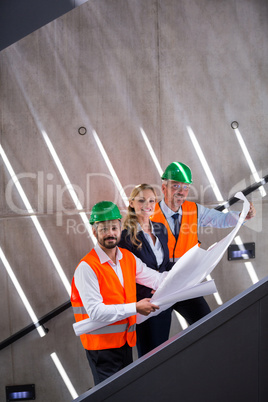 Businesswoman and architects standing on a staircase discussing with blueprint