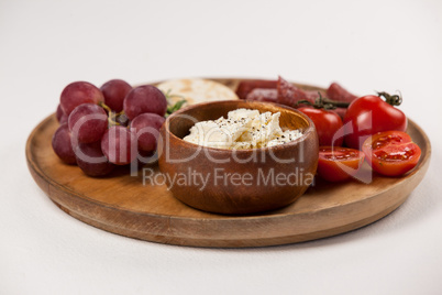 Crispy biscuits, cherry tomatoes, grapes and bowl of cheese on wooden board