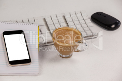 Cup of coffee with keyboard, mobile phone and mouse