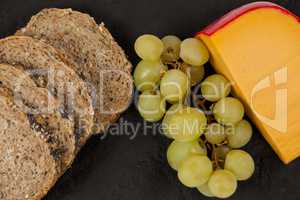 Slices of brown bread, grapes and gouda cheese on slate board