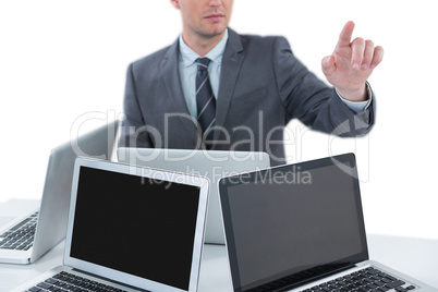 Businessman gesturing while sitting at table with four laptops