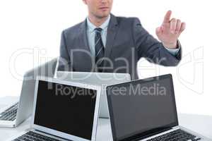 Businessman gesturing while sitting at table with four laptops