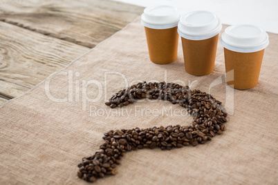 Coffee beans arranged in question mark shape with disposable coffee cups