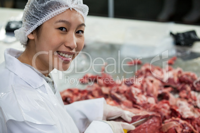 Female butcher cutting meat at meat factory