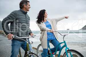 Happy couple on bicycle pointing at distance on beach