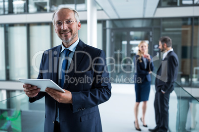 Portrait of businessman holding digital tablet and colleagues talking in background